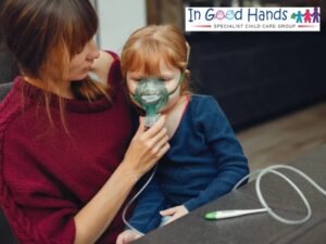 A woman assists a young child wearing a nebulizer mask, holding the mask to the child's face. A thermometer is in the foreground, and the logo for "In Good Hands SPECIALIST CHILD CARE GROUP" is in the top right.